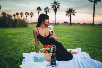 Chica morena guapa de picnic leyendo un libro y tomando vino con flores en un cesped cerca de la...