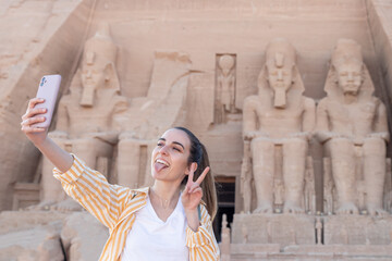 Young woman tourist taking a selfie with tounge out and peace out sign in Abu Simbel temple, Egypt