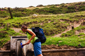 A woman at the water font refilling her water bottle during the Camino de Santiago