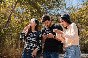 Multi-ethnicity group of best friends hiking using technology smartphone finding map pointing direction, Caucasian and Asian tourist lost in forest and trying find way ou