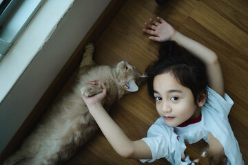 Little girl relaxing on the floor with her kitten. High angle view.
