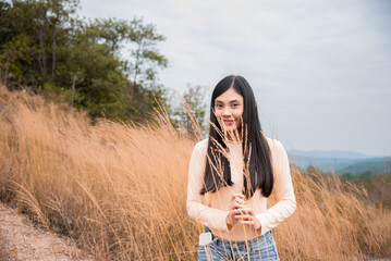 Happy young Asian woman smiling stand in golden meadow summer flower grasses field, beautiful girl enjoys traveling alone or exercising jogging, lifestyle freedom traveling outdoor vacation trip