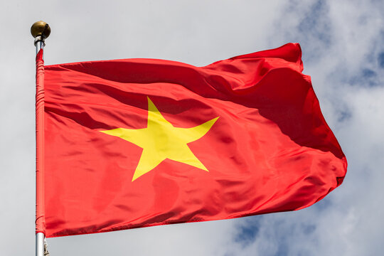flag of Vietnam flies against a clear blue sky with white clouds. Close-up, perfect for news