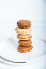 Stack of delicious freshly baked caramel, coffee and vanilla flavoured macaron confections on white plate against white background. French sweet food speciality.