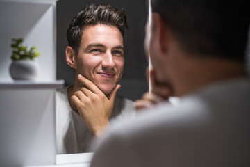 Portrait of man looking himself in a mirror while standing in bathroom.	