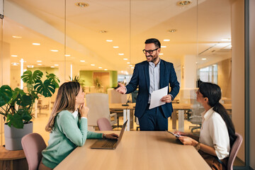 Businessman having a meeting with female colleagues, standing at the office, elegantly dressed.