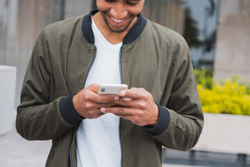 Happy ethnic man browsing smartphone on street