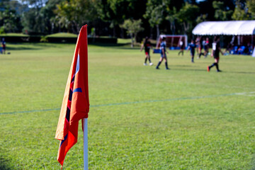 Orange corner flag from a football pitch, seeing group of players, coaches, staffs and parents...