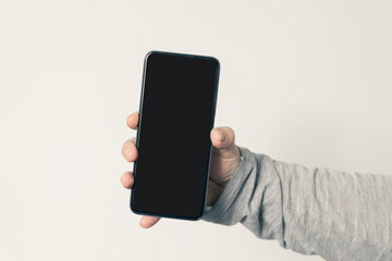 HAND HOLDING CELL PHONE WITH BLACK SCREEN ON WHITE BACKGROUND