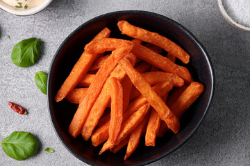 The concept of vegetarian cuisine and healthy eating is exemplified by the presentation of sweet potato sticks in a black bowl, accompanied by a white sauce.