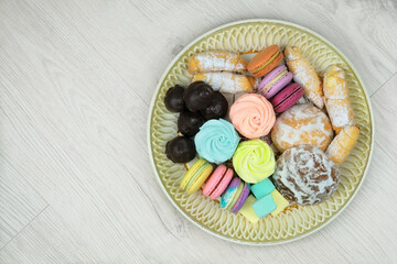 Sweet desserts in plate for the holiday on wood background. Marshmallows, macaroons, cake and chocolate candies in a large plate. Top view.