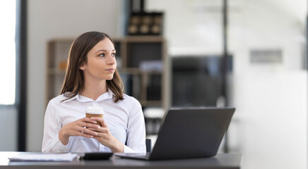 Beautiful young Asian businesswoman smiling holding a coffee mug and laptop working at the office.