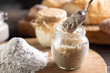 Active yeast freshly ripened on a spoon, smooth flour next to it and fresh bread in the background.
