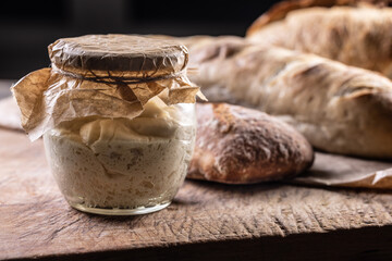 Rye sourdough ripened in a jar together with fresh bread on a cutting board.