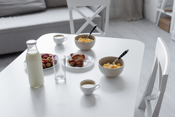 high angle view of glass bottle with milk near cups with coffee and tasty breakfast on table in kitchen.