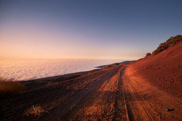 Fototapeta premium Dirt road in mountains above clouds at beautiful sunset. Tenerife, Canary Islands..