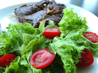 Serving for meat from fresh tomato halves on lettuce leaves drizzled with olive oil

