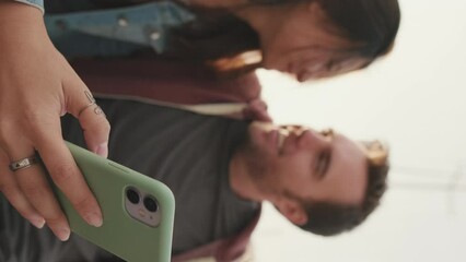 VERTICAL VIDEO: Close-up of young woman's hand holding smartphone. Girl and boy out of focus