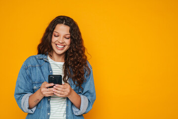 Young girl using smartphone isolated over yellow background