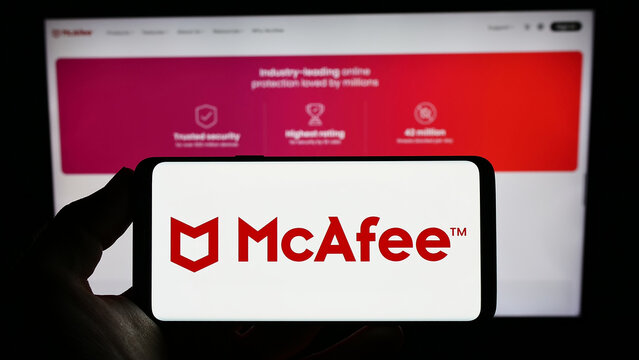 Stuttgart, Germany - 01-21-2023: Person holding smartphone with logo of security software company McAfee Corp. on screen in front of website. Focus on phone display.