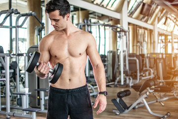 Fototapeta na wymiar Young man lifting dumbbell and working out on his biceps at gym.