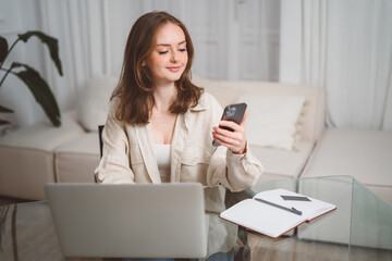 Young happy business woman, smiling pretty professional businesswoman worker looking at smartphone using cellphone mobile technology working at home or in office checking cell phone sitting at desk.