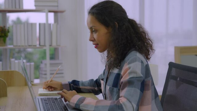 Young black mixed race woman study on distance take notes of online trainer teacher coach lecture course in web app. American lady online webinar client engaged in remote learning.