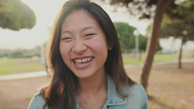 Close up, laughing young woman posing at camera while standing in park