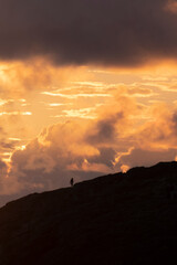 A lonely person silhouette rising a cliff at sunset