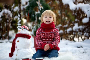 Fototapeta na wymiar Sweet blond toddler child, boy, playing in garden with snow, making snowman, happy kid winter time