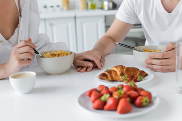 cropped view of young couple holding hands near delicious breakfast on table.