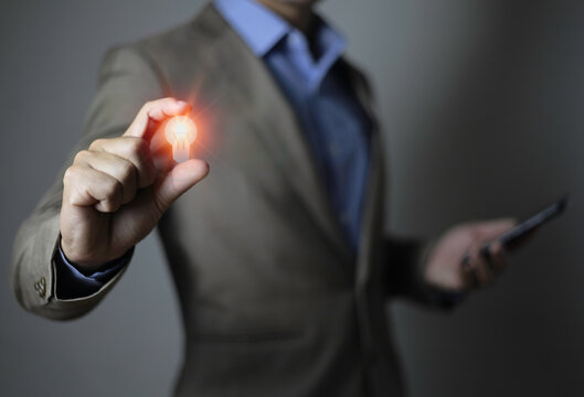Businessman in a suit with a light bulb in his hands. Holds a phone smartphone tablet glowing idea icon in his hand