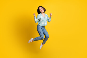 Fototapeta na wymiar Full length photo of girlish nice satisfied girl wear blue cardigan jeans clenching fists jumping isolated on yellow color background