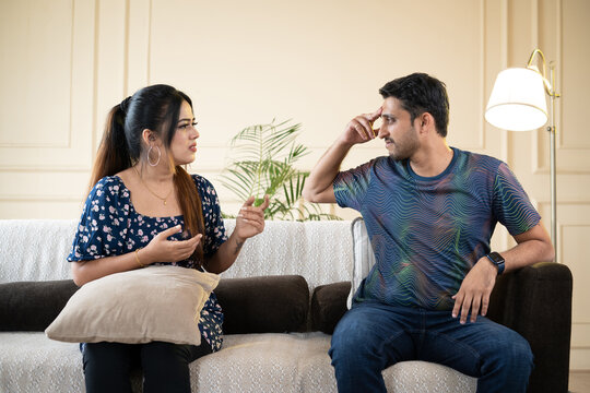 Angry indian couple fighting by shouting and arguing eachother while sitting on sofa at home - concept of break up, divorce and family problems