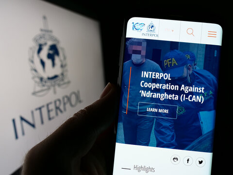 Stuttgart, Germany - 01-22-2023: Person holding cellphone with webpage of International Criminal Police Organization (ICPO) on screen with logo. Focus on center of phone display.