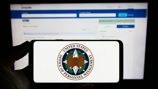 Stuttgart, Germany - 01-22-2023: Person Holding Cellphone With Seal Of US Office Of Personnel Management (OPM) On Screen In Front Of Webpage. Focus On Phone Display.