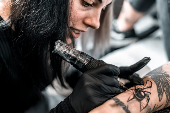 Professional young tattoo girl in black gloves making a black spider tattoo on the girl arm - Close Up of tattooer artist at work - Ink, draw and coloured skin lifestyle concept