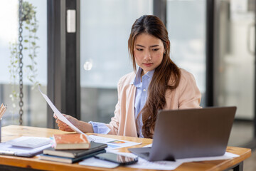 Thai Asian businesswoman working inside office with documents and laptop, worker paperwork calculates financial indicators smiling and happy with success and results of achievement and work