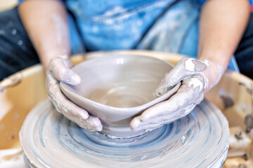 Close up hands make dishes from ceramic clay working on potters wheel traditional pottery craft