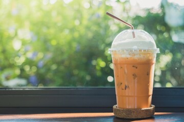 Side view of Ice thai milk tea on plastic cup on the wooden bar table with window, blur bokeh background in coffee shop