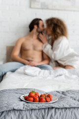 Obraz na płótnie Canvas plate with fresh strawberries near blurred sexy couple on background.