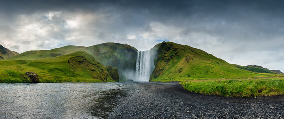 Panorama view of majestic Skogafoss waterfall flowing and moody sky in summer at south of Iceland