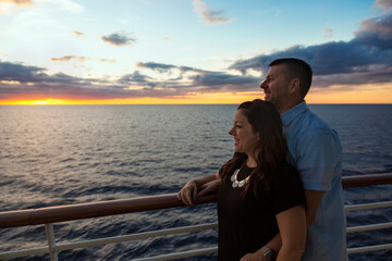 Attractive middle-aged couple enjoying the sunset view from the deck of a cruise ship while on a romantic vacation together