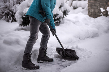 A boy with snow shovel is cleaning yard. Winter shoveling. Removing snow after blizzard.