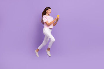 Fototapeta na wymiar Full size profile portrait of excited schoolgirl jump run use telephone empty space isolated on purple color background