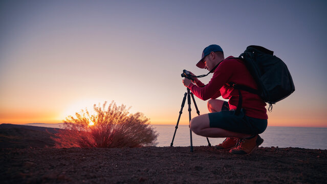 Photographer with camera on tripod at sunset. Man during photographing beautiful mountain landscape above clouds..