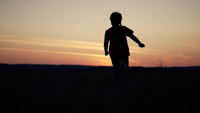 Little girl runs on the green grass. Happy child in a nature park at sunset. A cheerful girl runs in the field. Happy cute child in nature. Sunset in the summer. Girl running on the grass at sunset