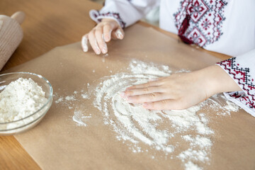 A girl in a national Ukrainian embroidered shirt pours flour on the table for making dough