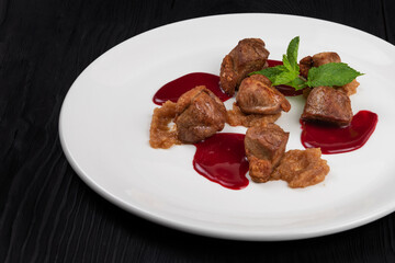 Pork meat with berries sauce and mint on white plate on wooden black background