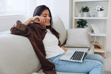 Obraz premium Woman freelancer on her day off sitting on the couch with a laptop at home and watching series and tv shows, smile